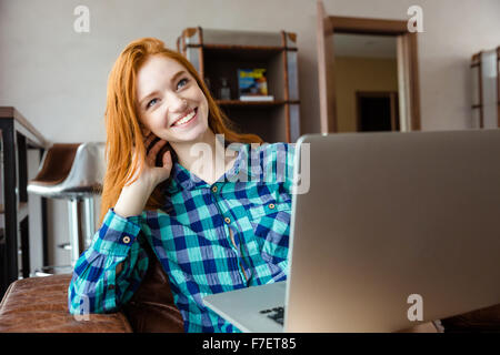 Felice bella ragazza redhead in plaid shirt ridendo e utilizzo portatile a casa Foto Stock