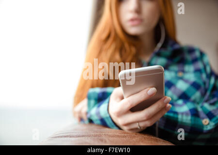 Vista dettagliata del cellulare è utilizzato da piuttosto pensieroso giovane donna redhead in plaid shirt Foto Stock