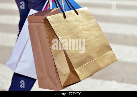 Primo piano di un giovane uomo caucasico portando alcuni di diversi tipi di carta shopping bags in strada Foto Stock