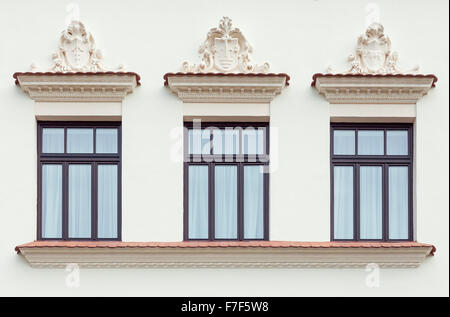 La facciata del palazzo e tre finestre decorate con stile classico e ornamenti di pietra Foto Stock