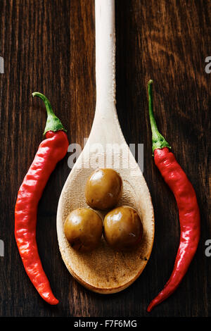 Le olive sul cucchiaio di legno circondato dal peperoncino e aglio Foto Stock