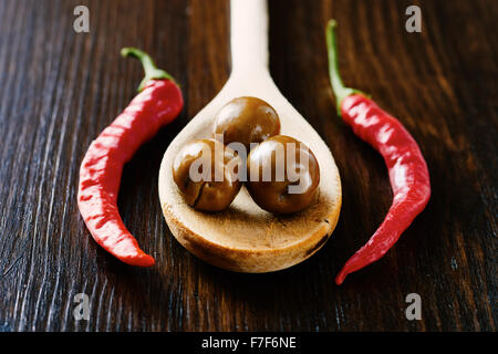 Le olive sul cucchiaio di legno circondato dal peperoncino e aglio Foto Stock