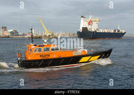 Arancione e nero barca pilota attraversando Portsmouth Porto di velocità con un traghetto roro caricato con contenitori in background Foto Stock