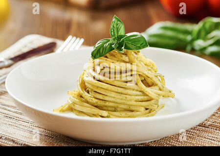 Pasta al pesto sulla piastra bianca circondata da ingredienti, sul tavolo di legno Foto Stock
