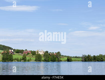 JAMTLAND, SVEZIA IL 07 AGOSTO 2015. Vista di terreni coltivati, lago e un villaggio rurale. Rosso di edifici di legno sul lato opposto. Editoriale. Foto Stock