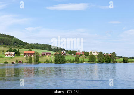 JAMTLAND, SVEZIA IL 07 AGOSTO 2015. Vista di terreni coltivati, lago e un villaggio rurale. Rosso di edifici di legno sul lato opposto. Editoriale. Foto Stock