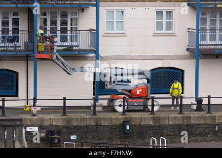 Due uomini con un cherry picker impresa di manutenzione su appartamenti a Goodheart posto, in Limehouse, Londra Foto Stock