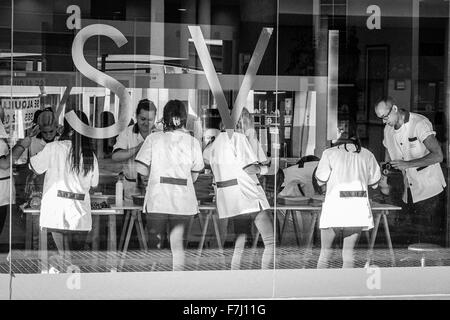 Benidorm, Spagna, parrucchieri studente di college partecipanti sui clienti visto attraverso la grande finestra Foto Stock