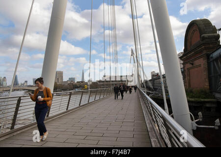 Una donna che guarda il suo smart phone a piedi attraverso uno dei Golden Jubilee piedi ponti sul fiume Thames, London, Regno Unito Foto Stock