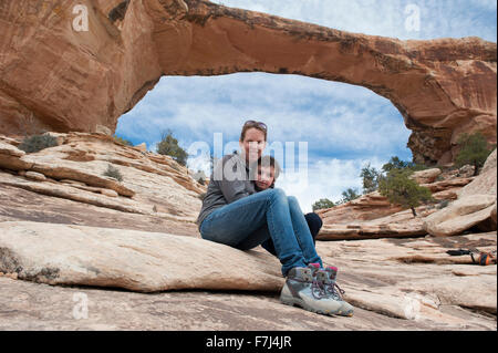 Madre e figlio seduti di fronte Owachomo Bridge, ponti naturali monumento nazionale, Utah, Stati Uniti d'America Foto Stock