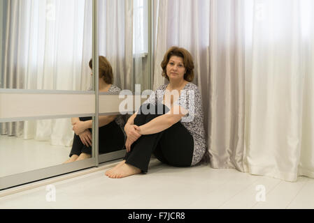 Premurosa donna seduta in un angolo della stanza sul pavimento Foto Stock