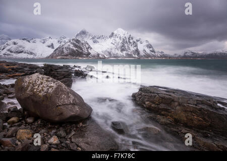 Montagne coperte di neve dietro dirupate lago freddo, Haukland Isole Lofoten in Norvegia Foto Stock