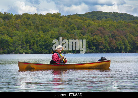 Senior l'uomo con il cappello, pesca da una piccola canoa sul lago Limekiln in Old Forge, New York. Lui è la bobinatura in un cast. Foto Stock