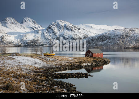 Capanna di pesca sulla baia di freddo al di sotto di montagne coperte di neve, Norvegia Foto Stock