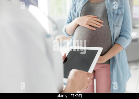 Medico con tavoletta digitale parlando a pazienti in stato di gravidanza Foto Stock