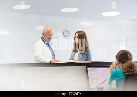 Il medico e il paziente adolescente discutendo medical record alla stazione di infermieri Foto Stock