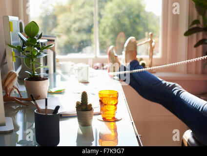 Donna che parla al telefono con piedi sulla scrivania in sunny home office Foto Stock