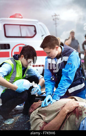 Gli operatori di soccorso di eseguire la rianimazione cardiopolmonare e la preparazione all'apparecchio per ventilazione di emergenza manuale su auto vittima di incidente Foto Stock