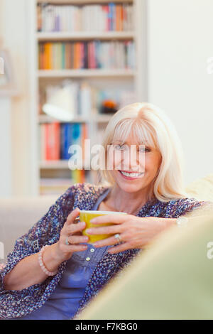 Ritratto sorridente donna senior di bere il caffè sul divano Foto Stock