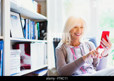 Sorridente donna senior texting in salotto Foto Stock