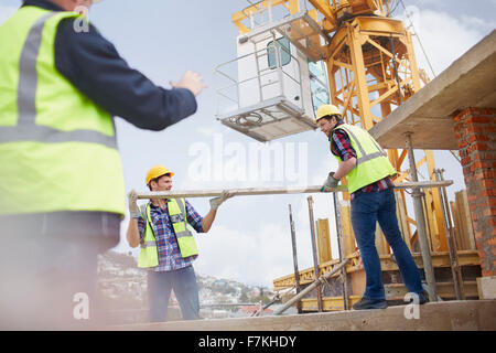 Lavoratori edili il sollevamento palo metallico sotto la gru al sito in costruzione Foto Stock