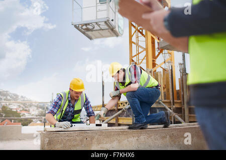 Lavoratori edili utilizzando lo strumento livello al sito in costruzione Foto Stock