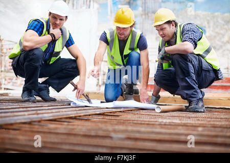 Lavoratori edili e ingegnere rivedendo blueprint al sito in costruzione Foto Stock