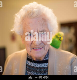 Una signora anziana in una casa di cura con un pet budgie sulla sua spalla Foto Stock