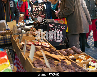 Piatti caldi e freddi preparati a mano poco costoso spuntini torte biscotti in vendita su occupato famoso West End, Covent Garden street food piazza mercato in stallo London REGNO UNITO Foto Stock