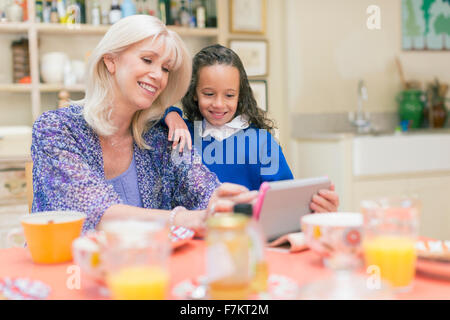 Nonna e nipote utilizzando digitale compressa al tavolo per la colazione Foto Stock