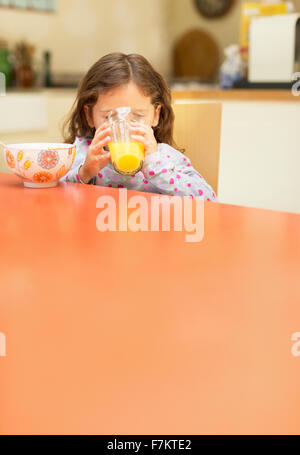 Ragazza di bere succo di arancia al tavolo per la colazione Foto Stock