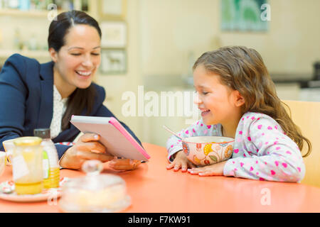 Madre e figlia utilizzando digitale compressa al tavolo per la colazione Foto Stock