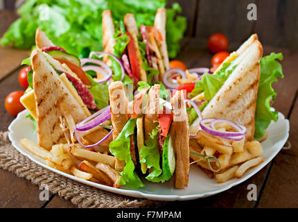 Club sandwich con formaggio, cetriolo, pomodoro, carne affumicata e salame. Servito con patate fritte. Foto Stock