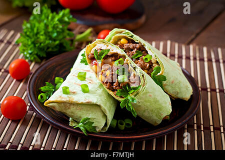 Burrito si avvolge con carne macinata e verdure su un sfondo di legno Foto Stock