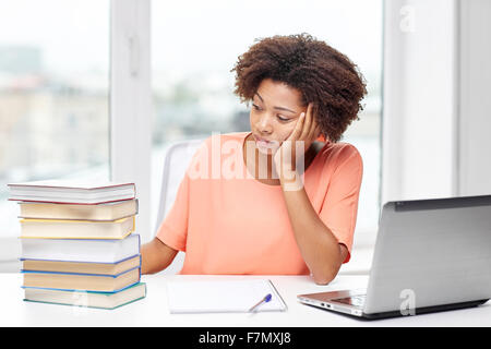 Annoiato americano africano donna facendo i compiti a casa Foto Stock