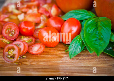 Tritate i pomodori ciliegini e basilico su un tagliere Foto Stock