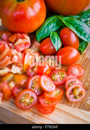 Tritate i pomodori ciliegini e basilico su un tagliere Foto Stock