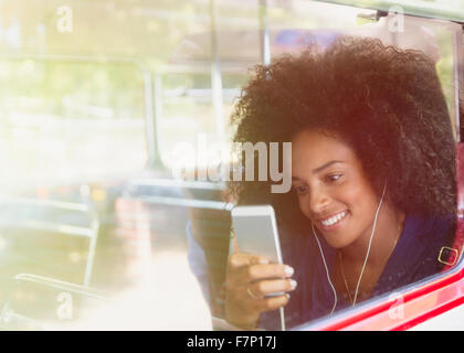 Donna sorridente con afro ascolto di musica con cuffie e lettore mp3 sul bus Foto Stock