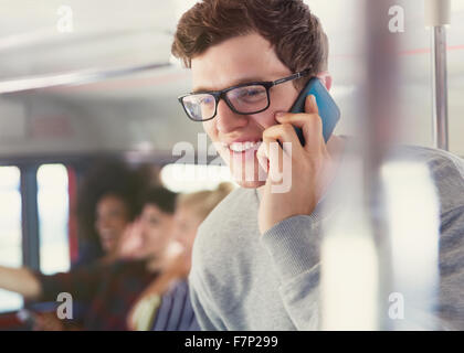 Uomo sorridente con occhiali parlando al cellulare sul bus Foto Stock