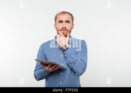 Ritratto di un uomo pensieroso azienda computer tablet e guardando in alto isolato su sfondo bianco Foto Stock