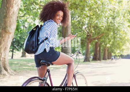 Ritratto di donna sorridente Bicicletta Equitazione con lettore mp3 e le cuffie in posizione di parcheggio Foto Stock