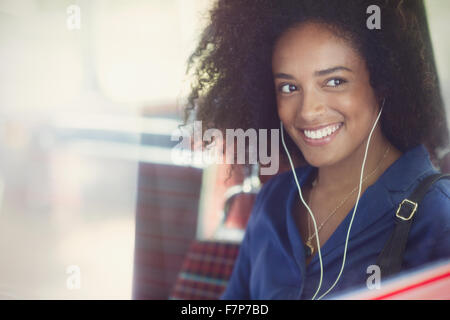 Donna sorridente con afro ascolto di musica con le cuffie sul bus Foto Stock