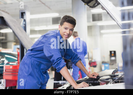 Ritratto meccanico fiducioso sporgendoti auto motore nel negozio di riparazioni auto Foto Stock