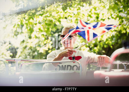 Donna sorridente sventola bandiera britannica su autobus a due piani Foto Stock