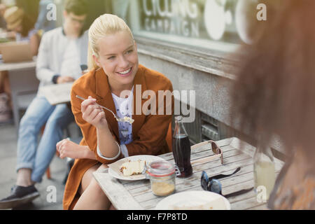 Sorridente donna bionda di mangiare il dessert al cafè sul marciapiede Foto Stock