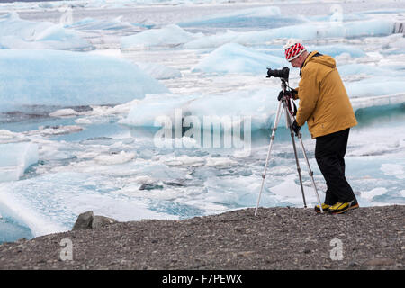 Fotografo con treppiede con blocchi di ghiaccio sulla spiaggia presso Jokulsarlon, Islanda in febbraio Foto Stock