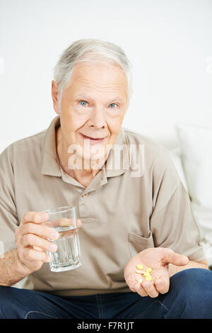 Uomo senior di assumere un farmaco con un bicchiere di acqua Foto Stock