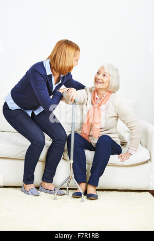 La donna aiuta donna senior con canna ad alzarsi da un divano Foto Stock