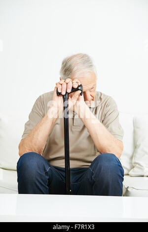 Triste uomo senior con canna seduto su un divano Foto Stock