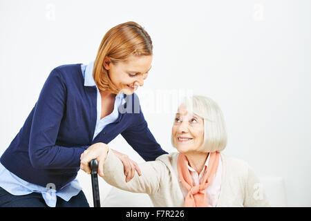 Il caregiver ad aiutare la donna senior con canna ad alzarsi da un divano Foto Stock